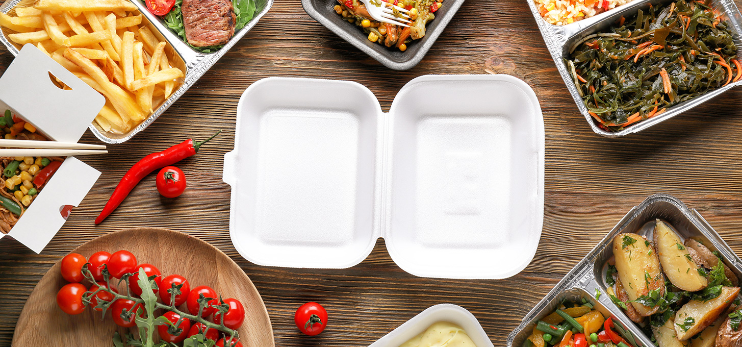 Different types of food containers including styrofoam, paper, and aluminum with food in them on top of a wooden table