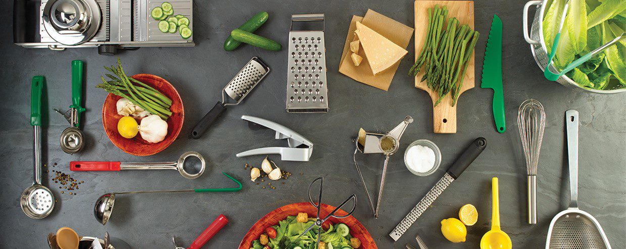 Countertop full of different types of small kitchen utensils including a whisk, bowls, measuring utensils, cheese graters, and a garlic press